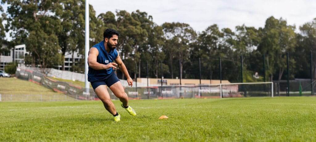 Male athlete in mid-sprint during agility cone drill on a sports field, focusing on speed and control.