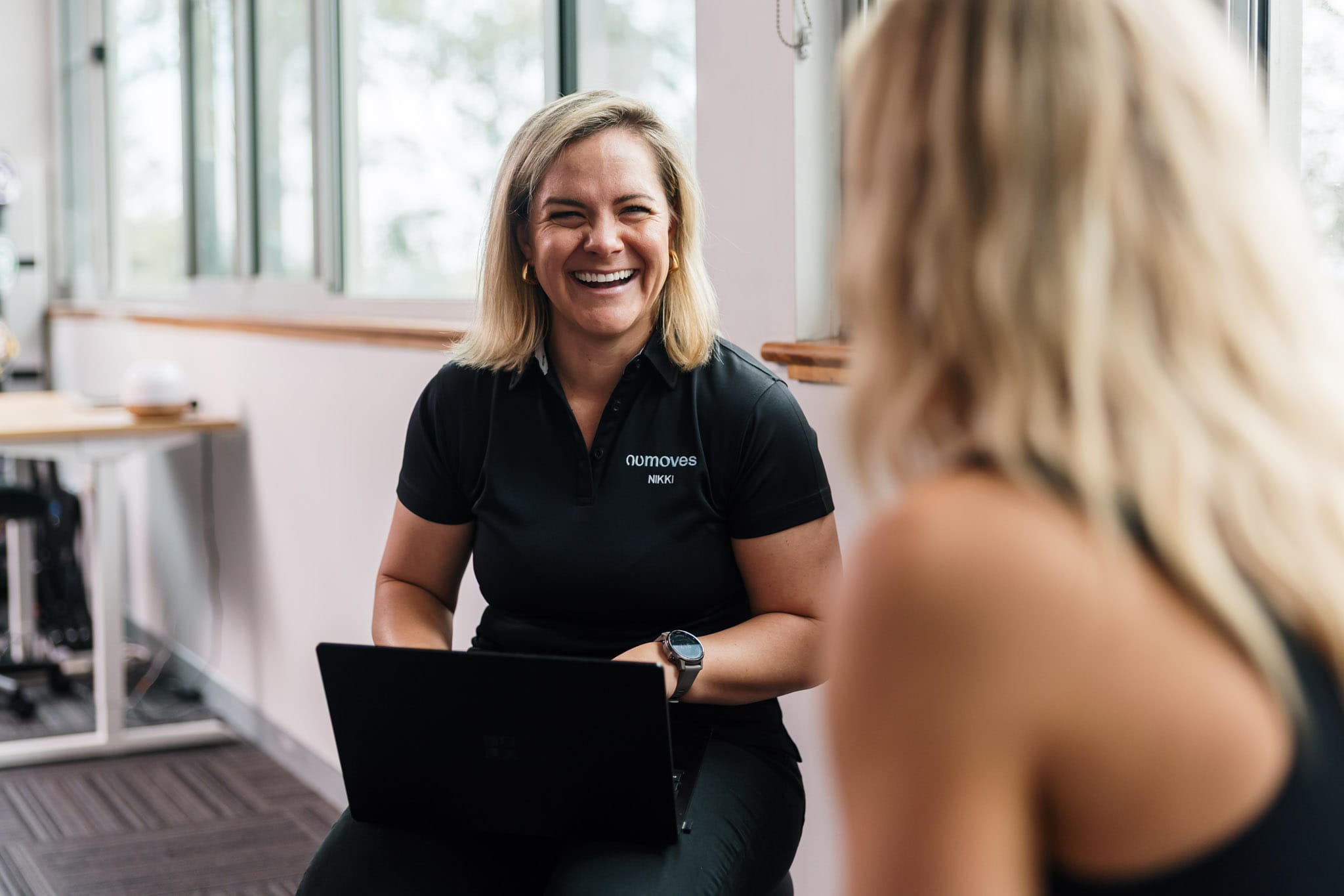Female physiotherapist named Nikki smiling and holding a laptop during a consultation with a client at NUmoves Physio.
