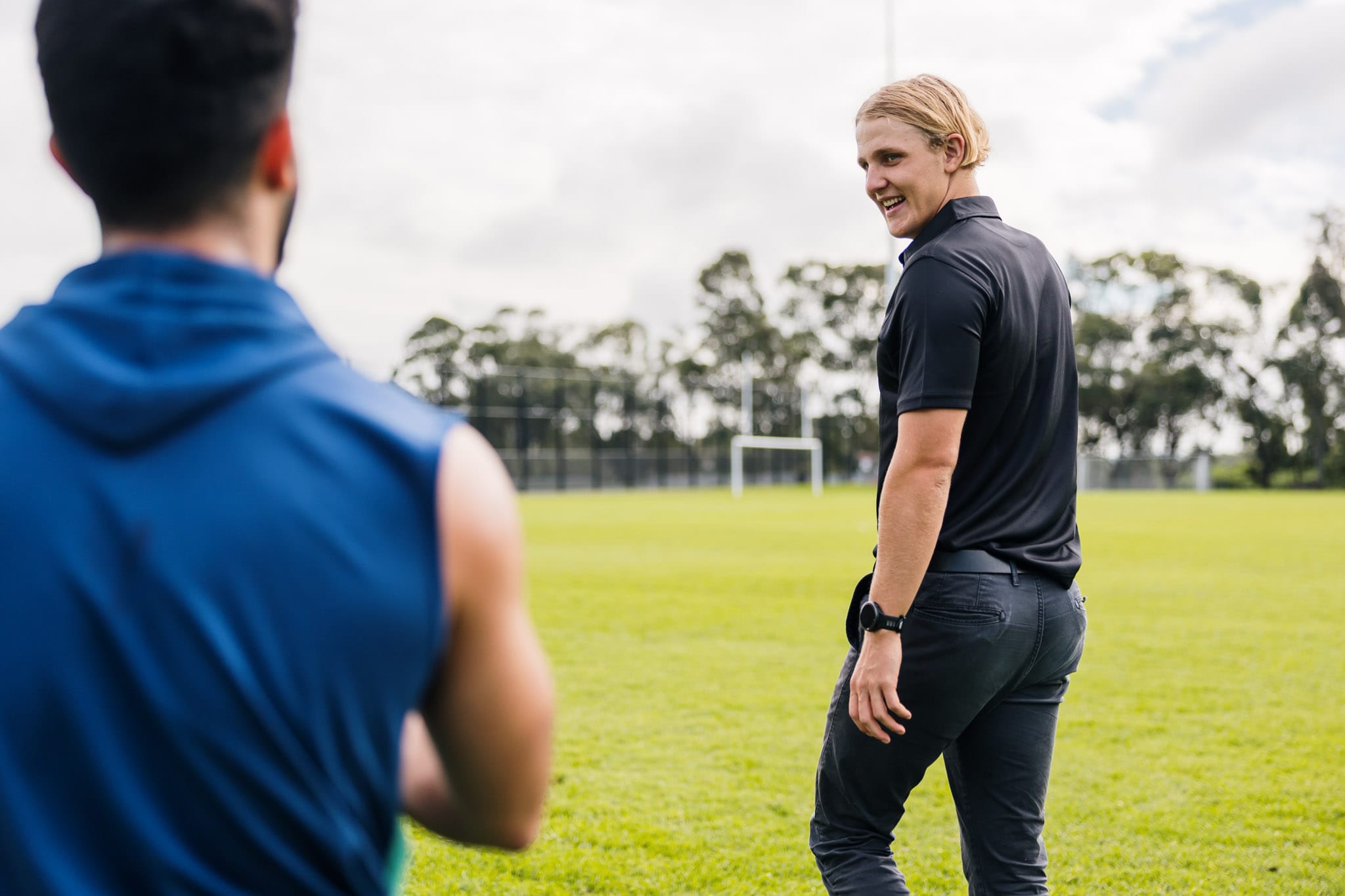 Young male physiotherapist smiling and engaging with an athlete on a sports field, ready to provide support or guidance.
